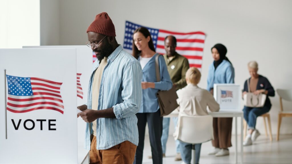 Multi-cultural, young voters at voting booths with American Flag on wall