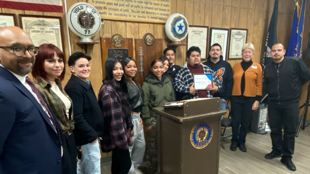 A dozen people, young and old, of various ethnicities behind a podium with Democracy Works Award