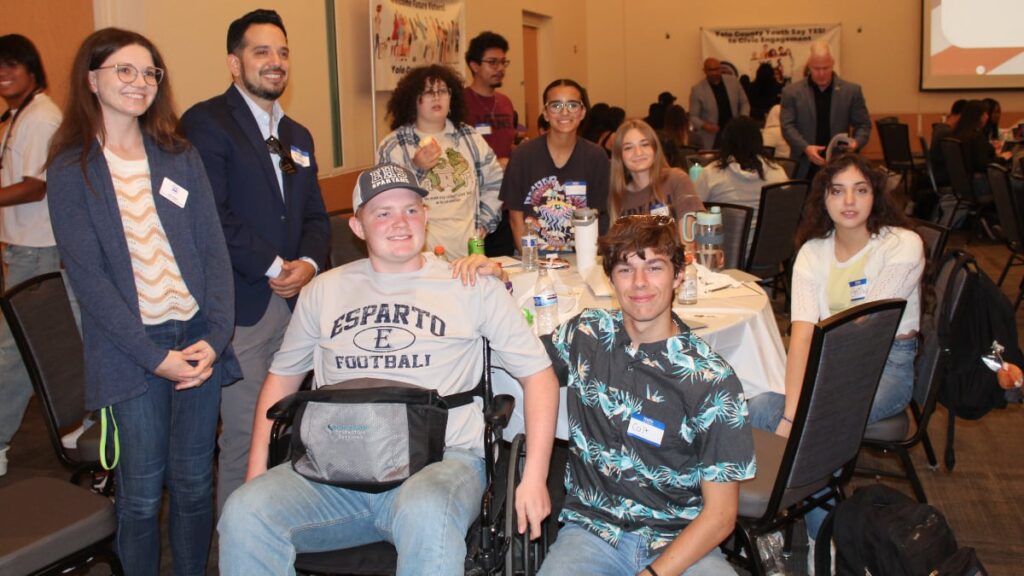 Yolo County Board Member, Angel Barajas overlooking table of students, one in a wheelchair at the 2024 Youth Empowerment Summit. 