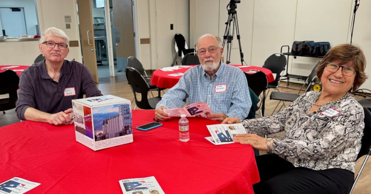 Three people seated at a round table with red tablecloth