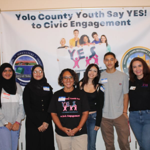 Gloria Partida, Davis councilwoman, with a diverse group of youth in front of a YES Civic Engagement banner