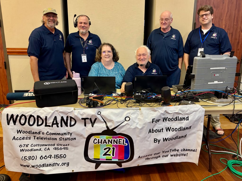 A TV crew posing behind a table of equipment and the Woodland TV banner