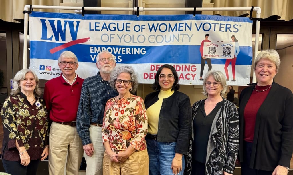 Seven people posing in front of a LWV banner