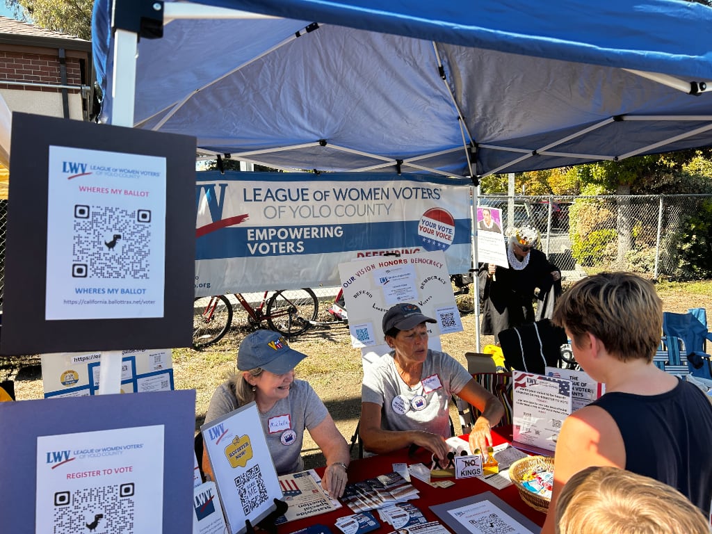 Two women with LWV ball caps at table kitted out with all sorts of voting info and encouragement