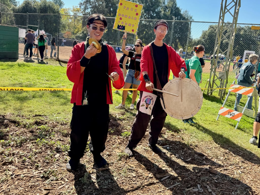 Two young, asian men drumming and cymbolling at No Kings rally entrance