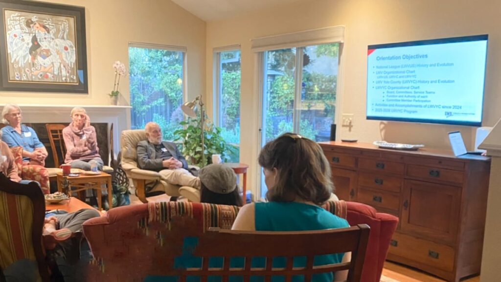 Six people in a living room watching the LWVYC orientation slides on a large TV monitor