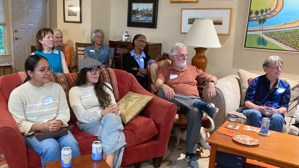 Eight people in a living room listening intently to someone off camera