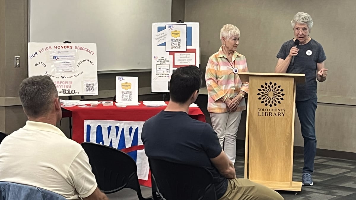 Two LWV members at a podium in front of two men in the audience