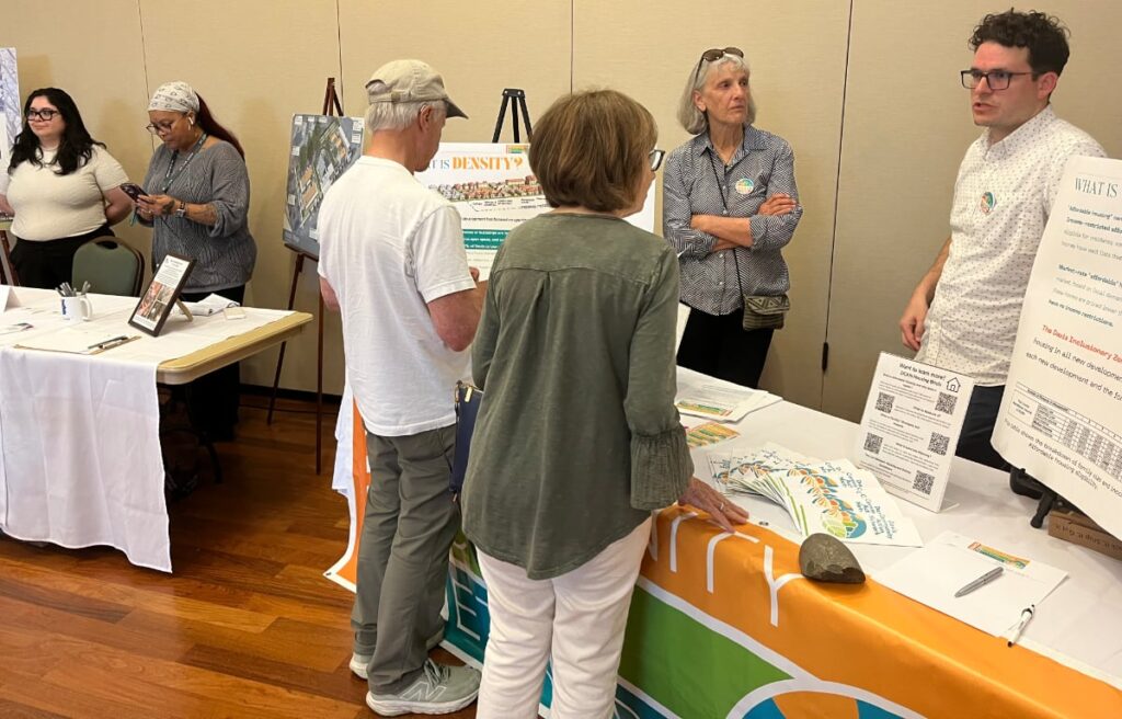 A woman speaks to a young man behind one of two tables with housing materials available.