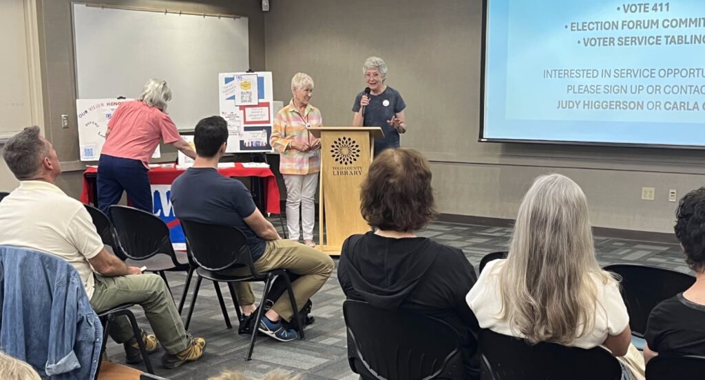 Two women at a podium with a screen behind describing LWV volunteer opportunities