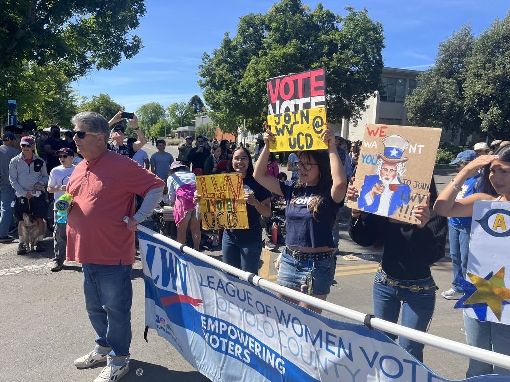 LWV of Yolo County friends and members holding a banner and VOTE signs on a Davis street in the Picnic Day Parade