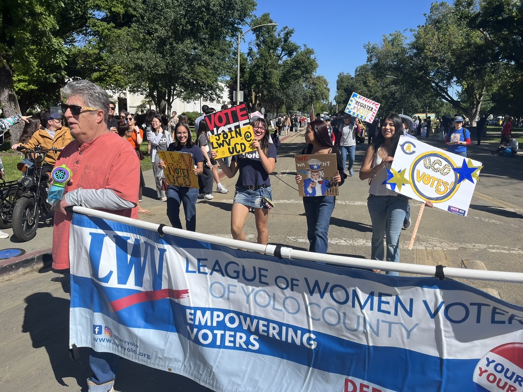LWV of Yolo County friends and members holding a banner and VOTE signs on a Davis street in the Picnic Day Parade