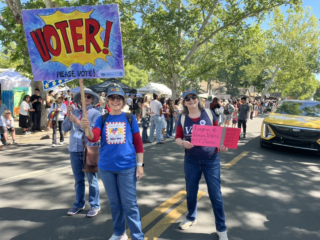 Two LWVYC Board Members holding signs and marching on a Davis street during the 2026 Davis Picnic Day parade