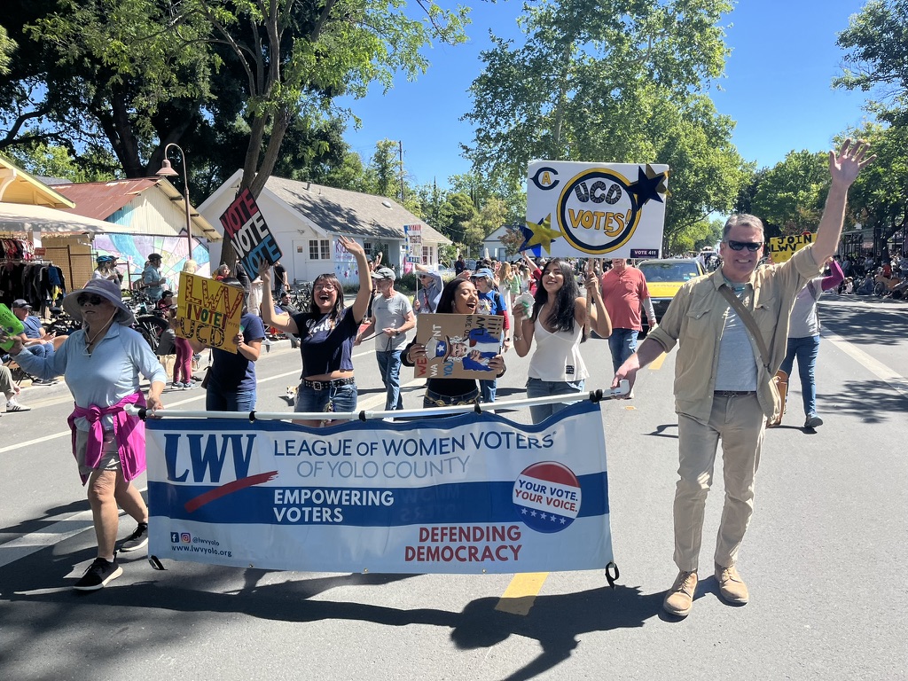 LWVYC members holding a banner, followed by UCDavis League Club students on a small town street in a parade