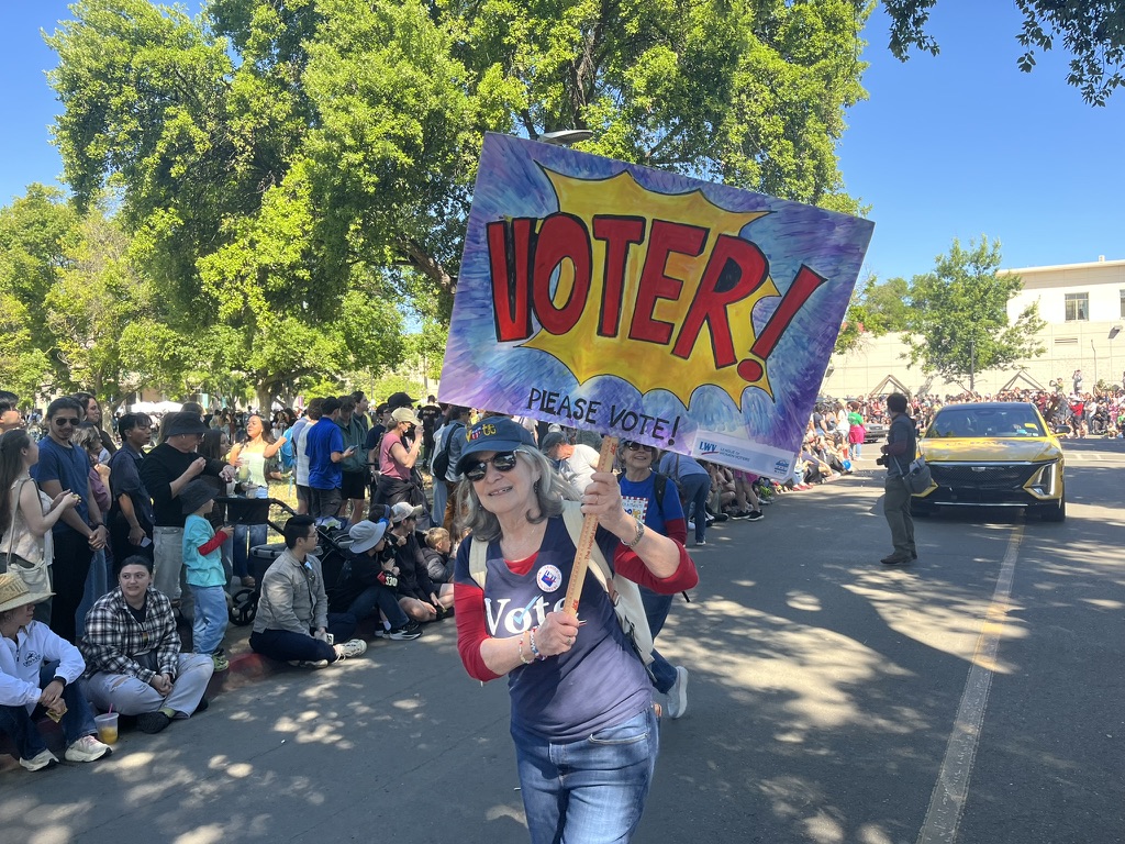 A woman with a large sign that says Voter! in a small-town parade with crowds of people along the side of the road