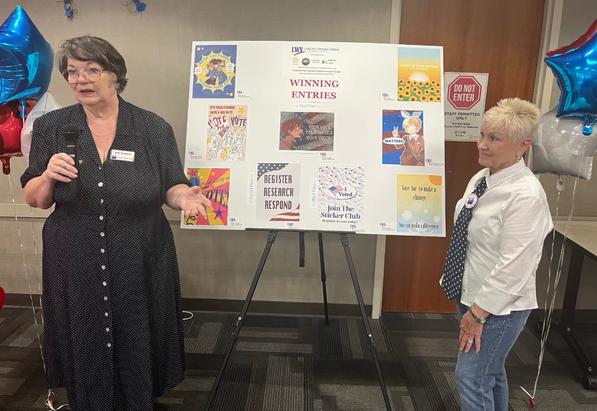 Two women in front of poster of art contest entries