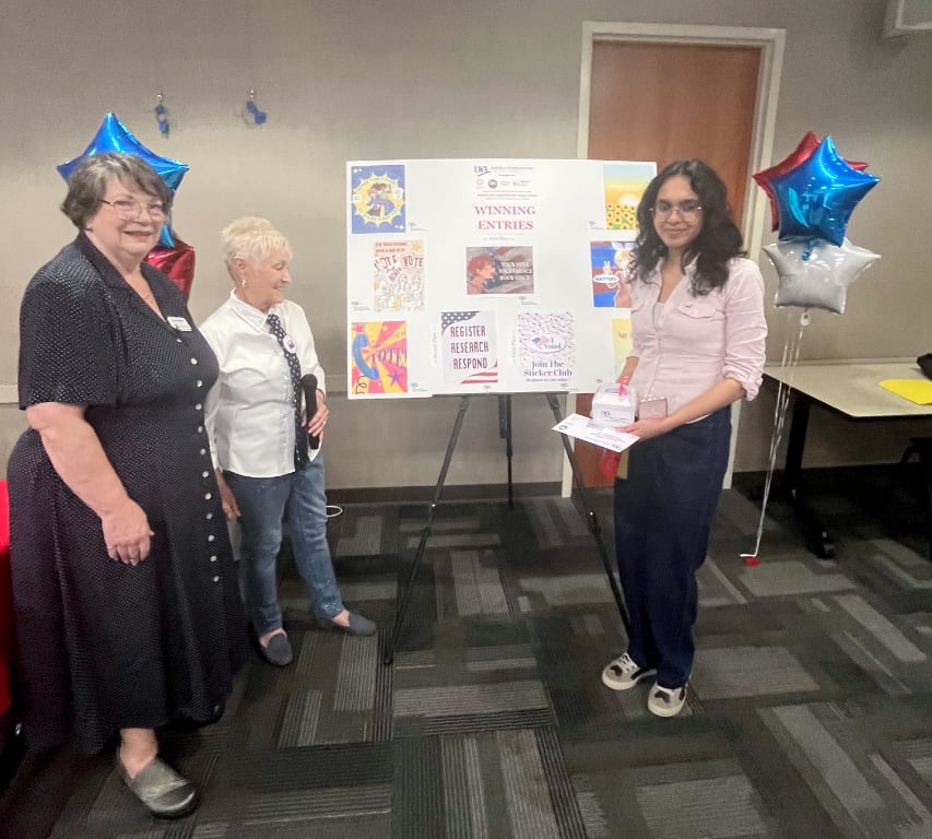 Two women and a high school student in front of a poster of art works