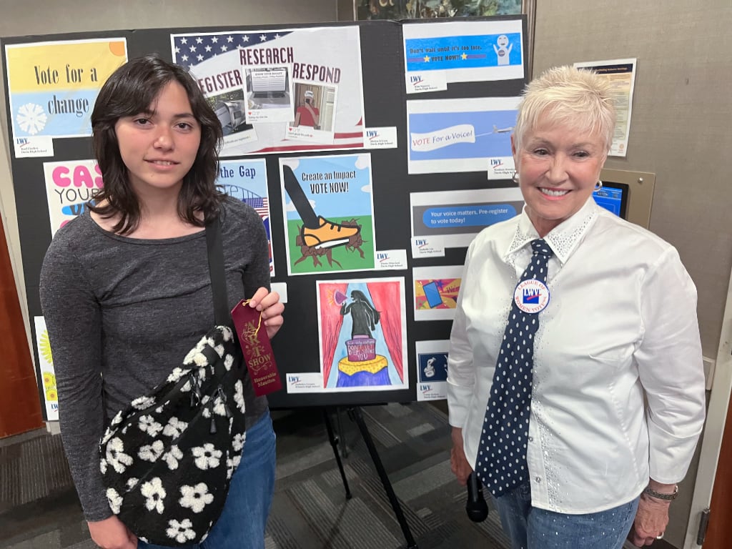 A League leader and high school student in front of poster of art projects