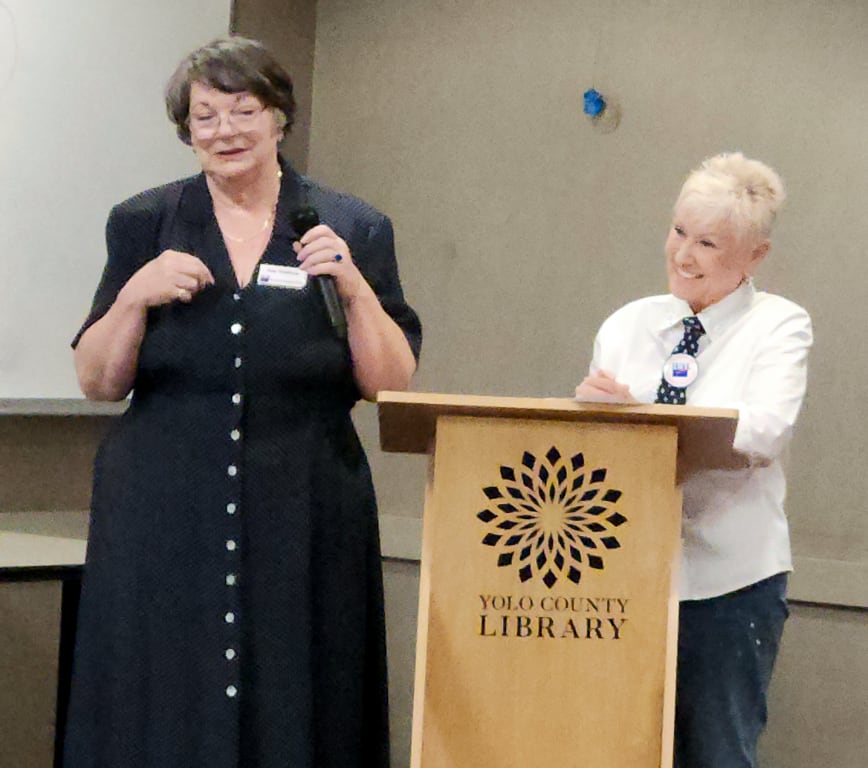 Two women at a podium with the Yolo County Library logo on the front.