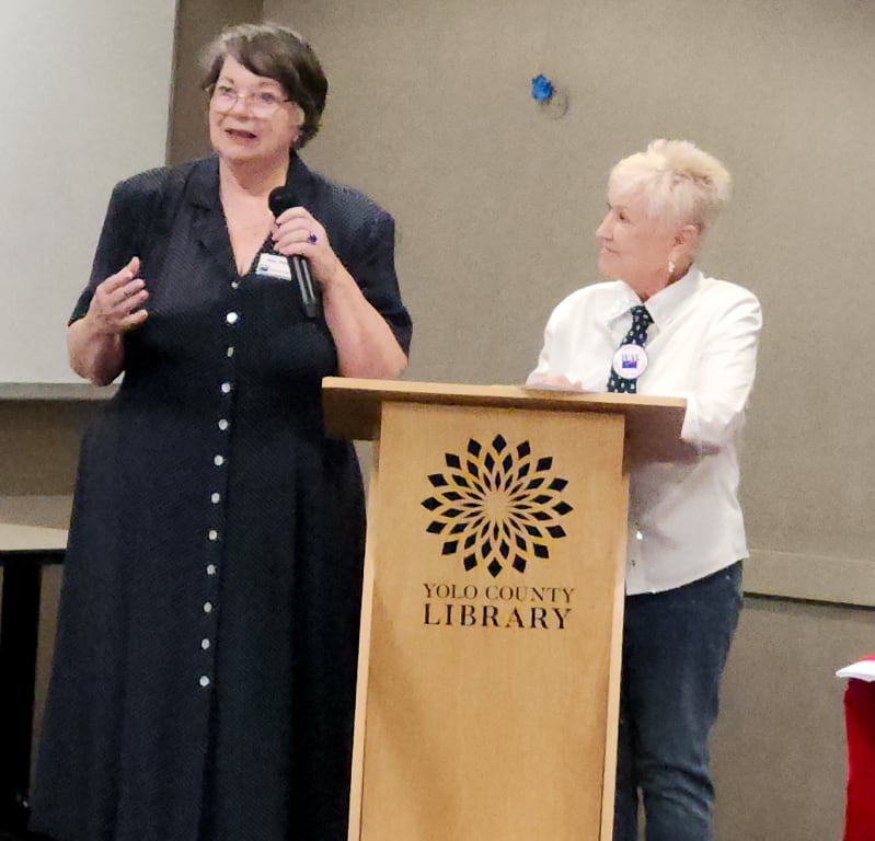 Two women at a podium with the Yolo County Library logo on the front.